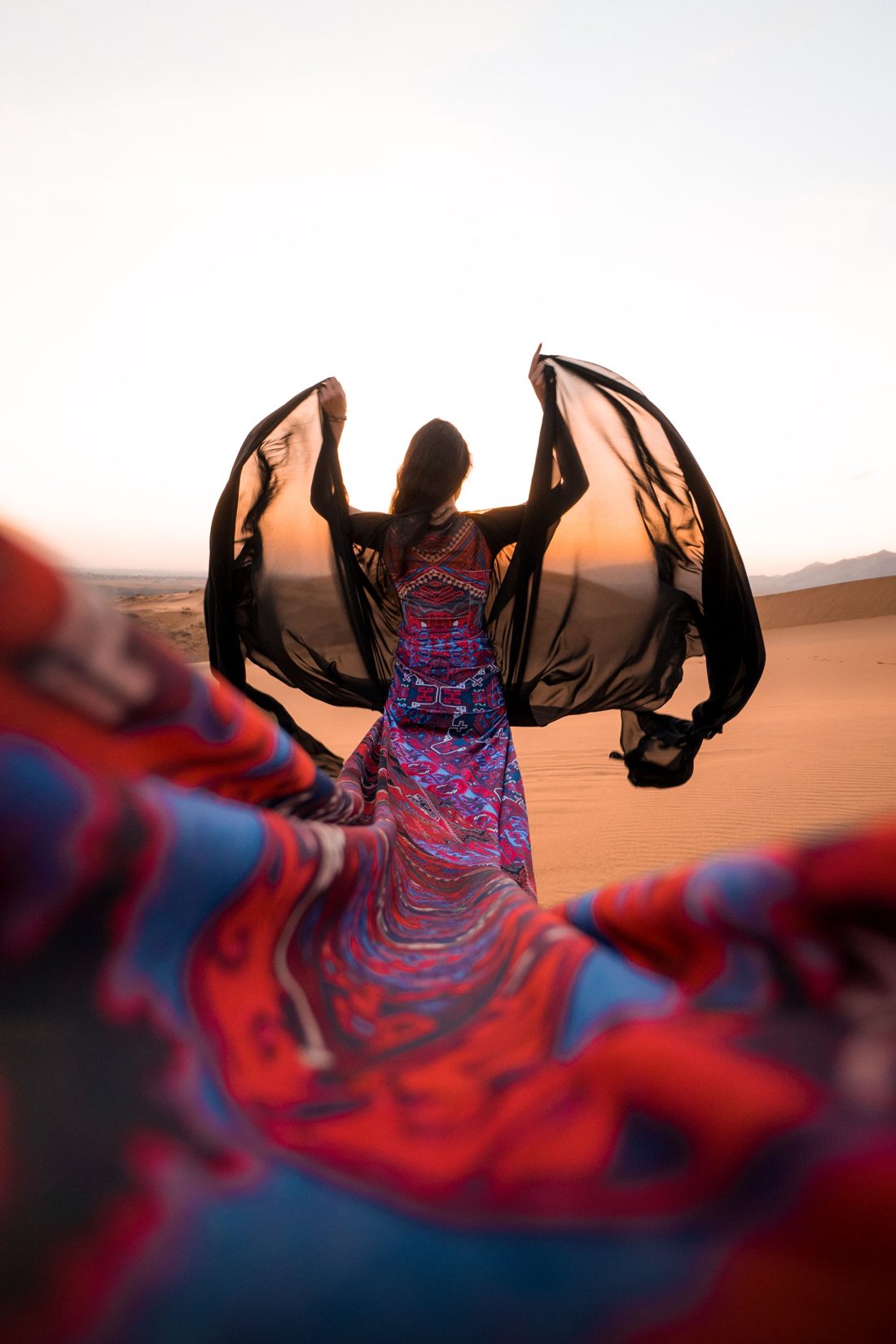 A woman in flowing textile crosses the dunes at dusk