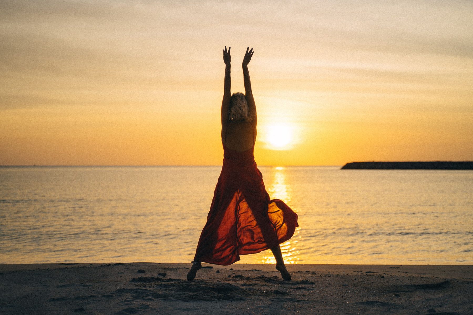 A woman on the shore at sunrise, arms raised to the light